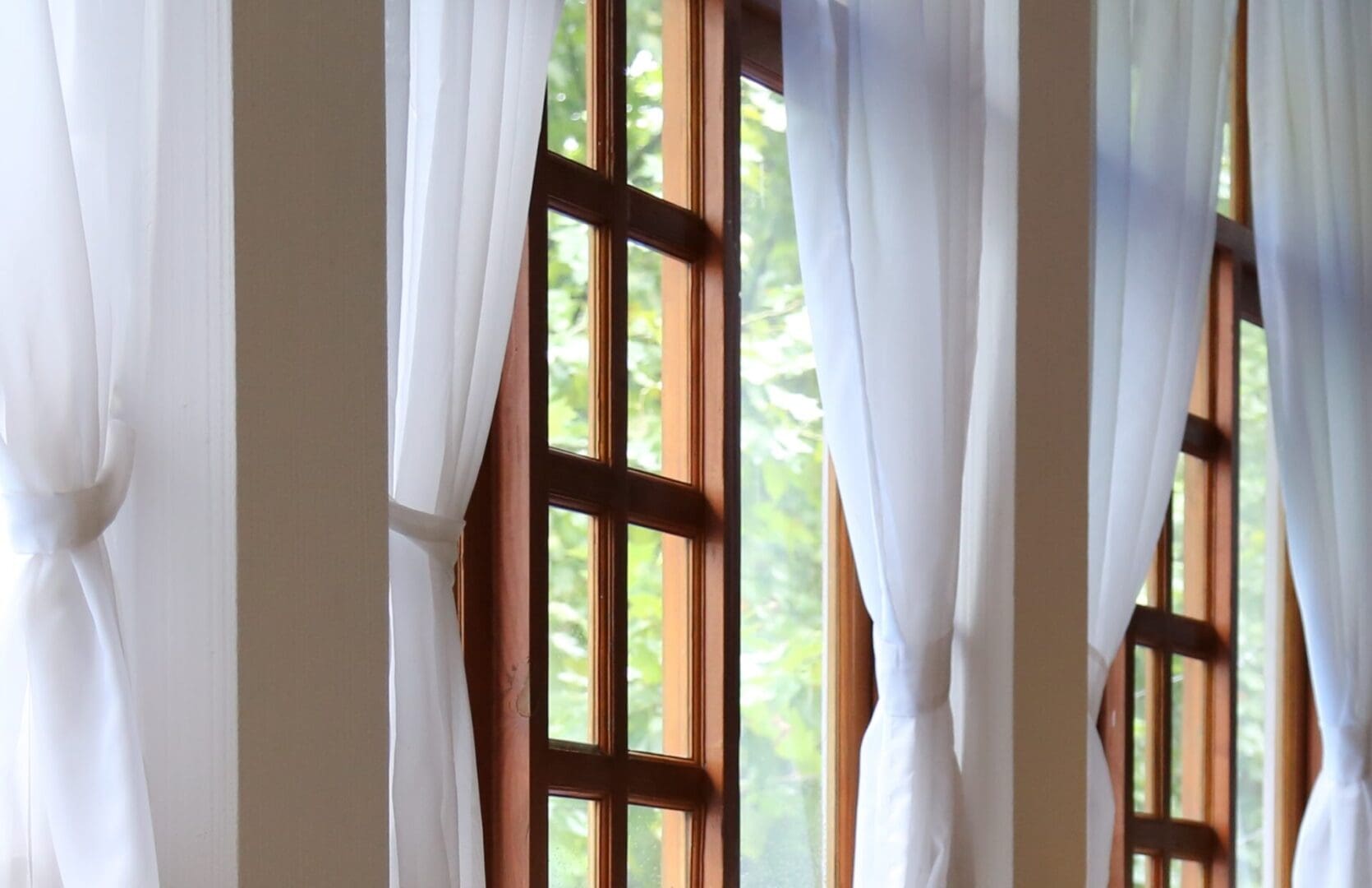 Sunlit wooden windows with sheer white curtains